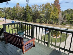 A wooden swing chair on a green deck with a view of a lake and trees.