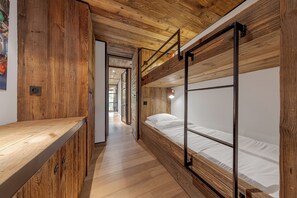 Un couloir étroit, avec un plancher et des murs en bois, qui mène à un lit superposé doté de barrières métalliques.