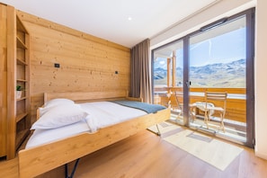 A wooden bed with a view of mountains through a glass door. - “V20” by Versant Collection (Val Thorens)
