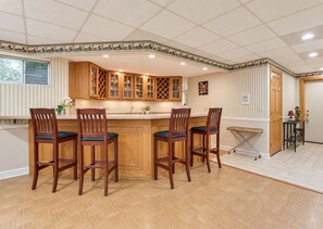 Una cocina con armarios de madera, una isla central con taburetes de bar y un techo decorativo.