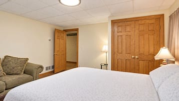 Habitación de hotel con una cama grande, un armario de madera, una mesita con una lámpara y un sofá con cojines.