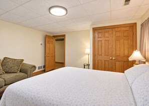 A hotel room with a large bed, a wooden wardrobe, a small table with a lamp, and a sofa with cushions. - Creekside Grand Lodge (Barrington)