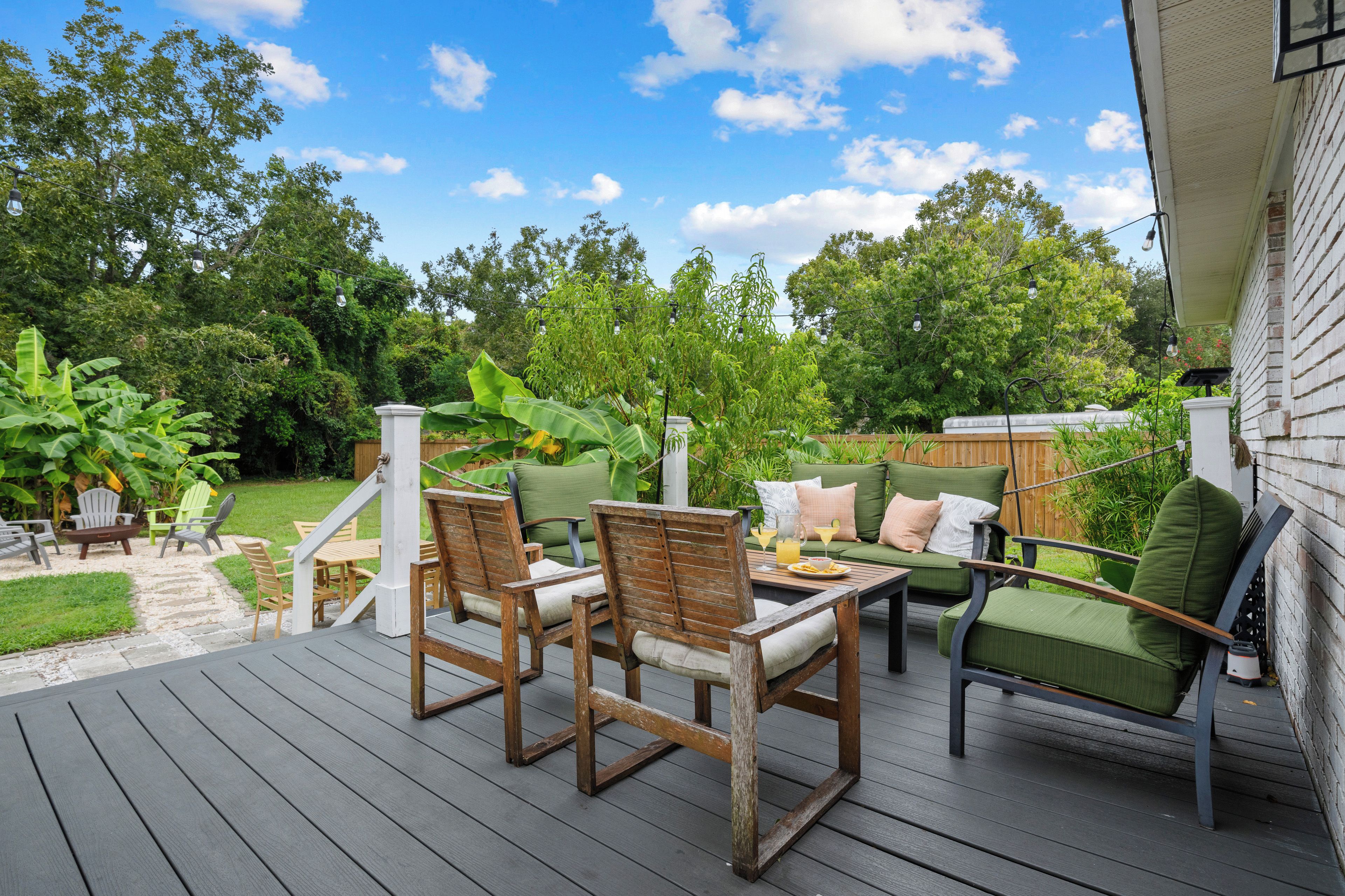 A deck with outdoor furniture, including chairs and a table, surrounded by lush greenery and trees.