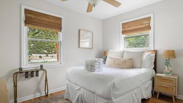 A bedroom with a bed, two bedside tables, a nightstand, a ceiling fan, and windows with blinds.