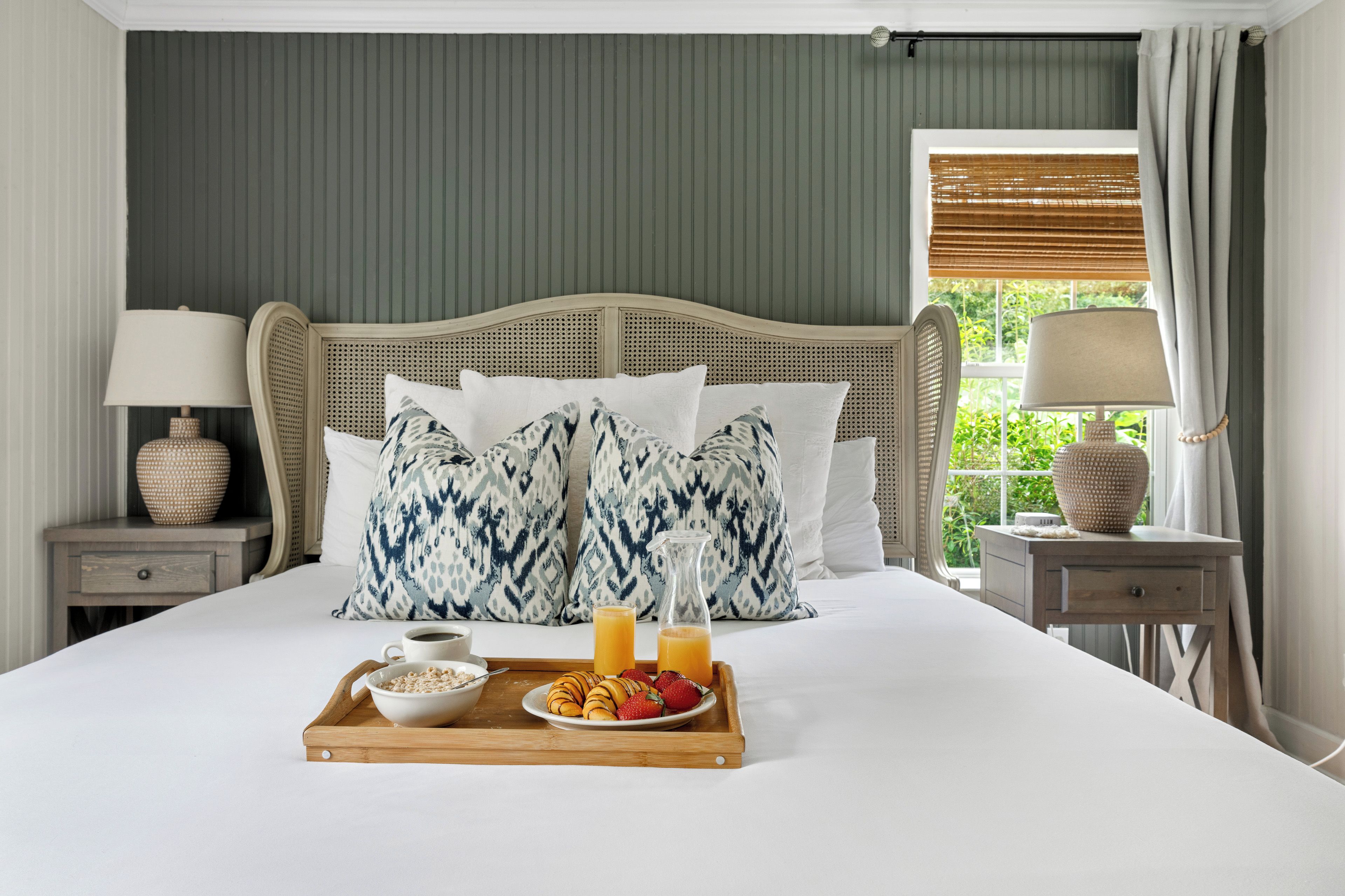 A neatly made bed with a tray of breakfast, including cereal, fruit, and juice.