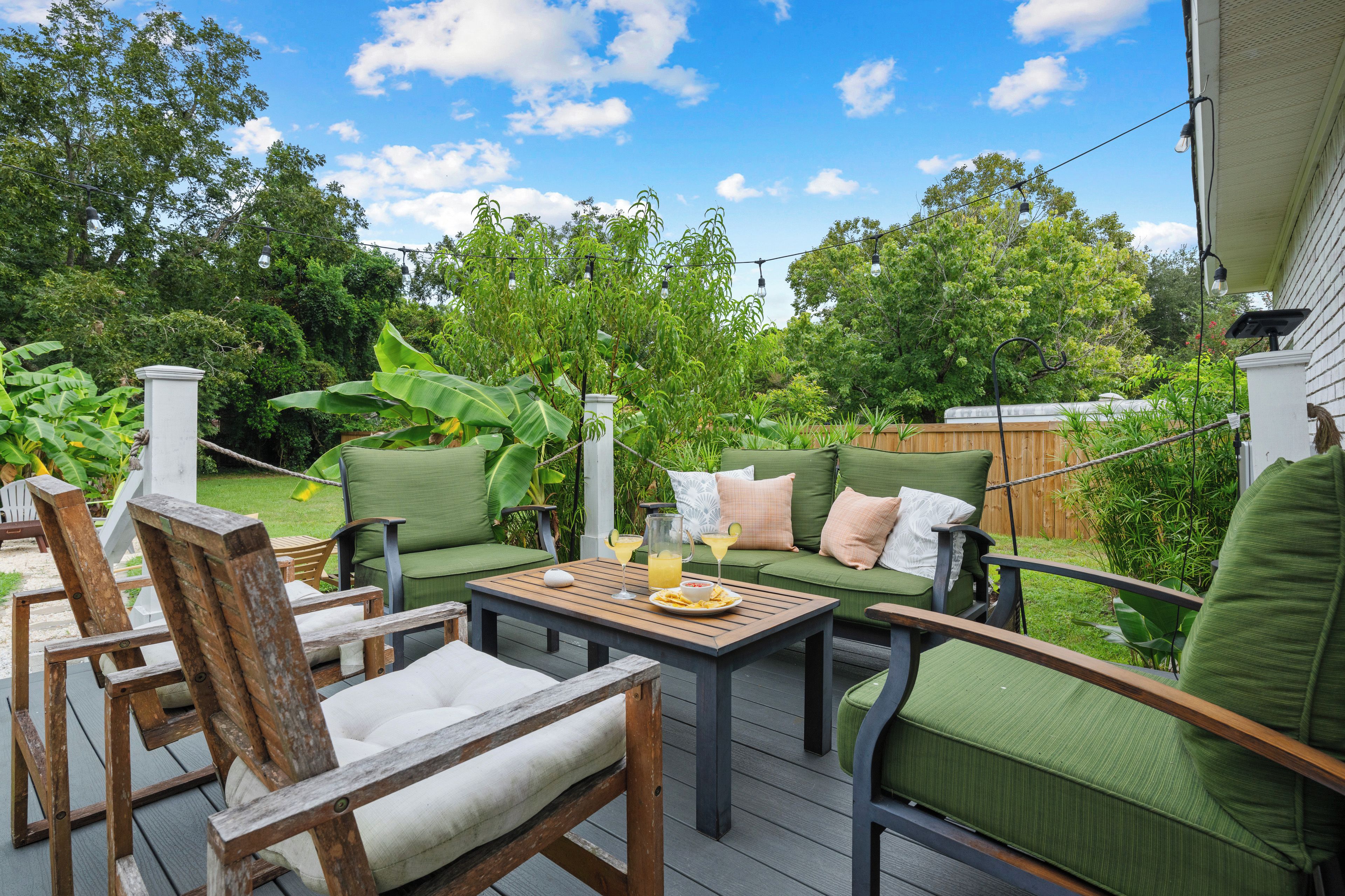 An outdoor patio with a wooden deck, green cushioned seating, and a table with drinks.