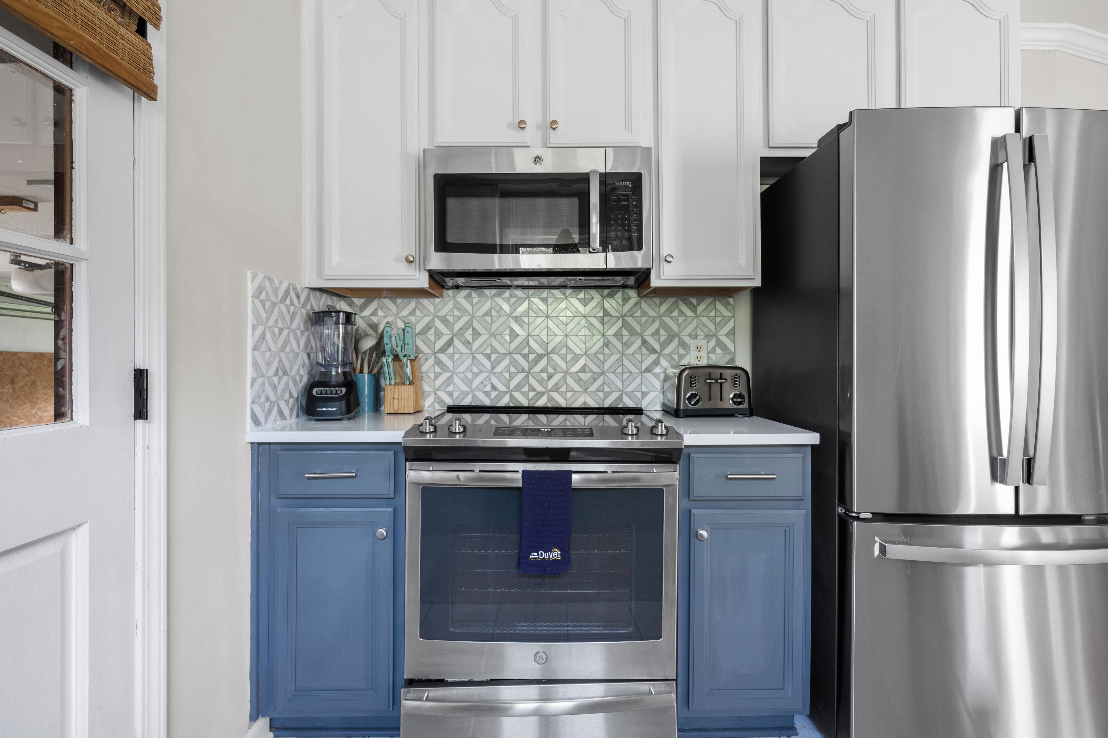 A kitchen with white cabinets, a stainless steel refrigerator, a microwave, a stove, and a toaster.