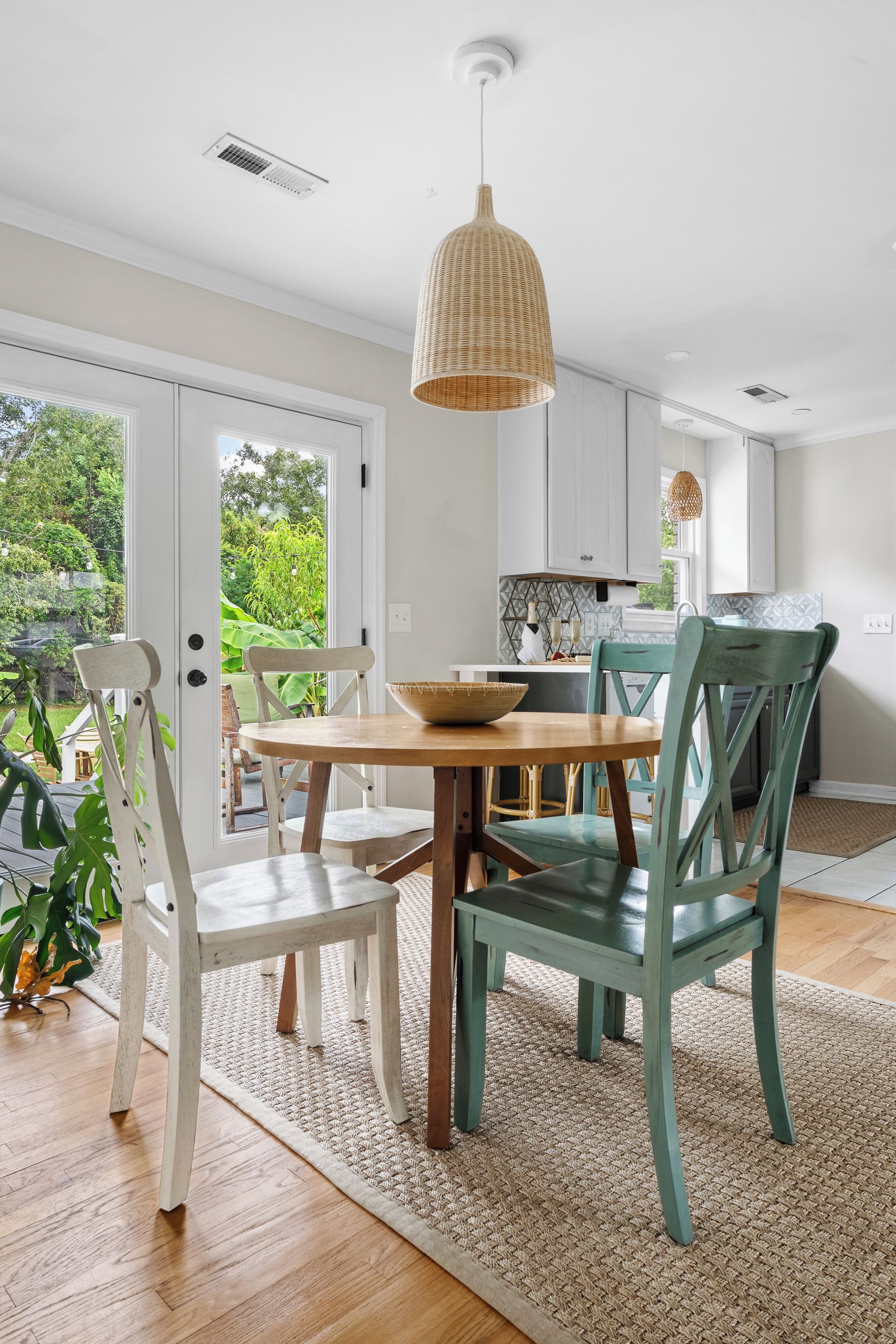 A dining area with a round table, chairs, a woven pendant light, and a view of greenery outside.