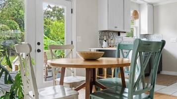 A dining area with a round table, chairs, a woven pendant light, and a view of greenery outside.