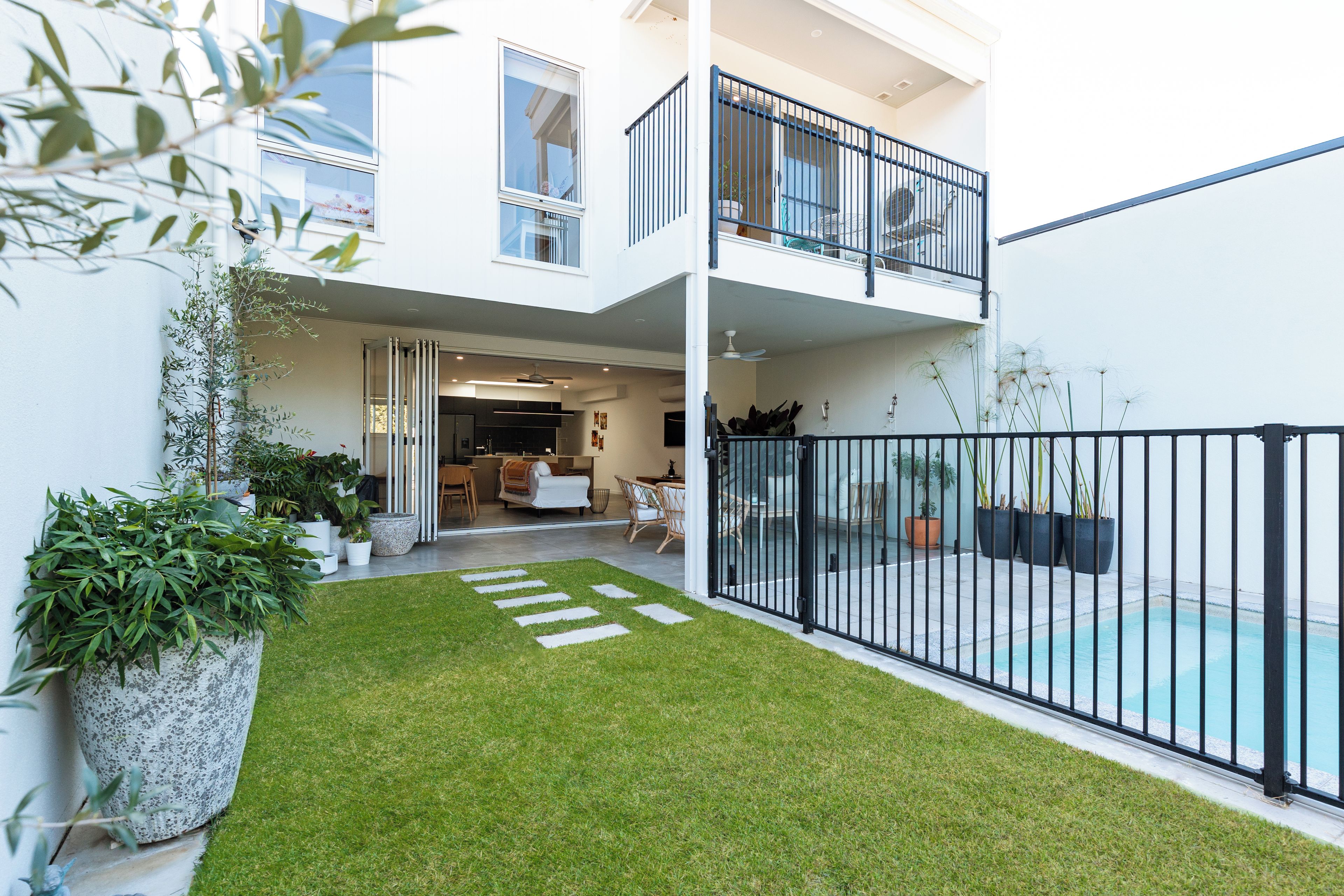 Un edificio residenziale moderno su due piani, con un balcone, una piscina e un prato curato.