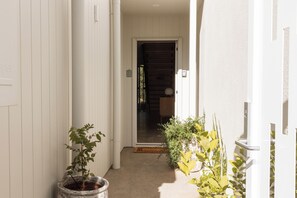 A narrow corridor with white walls, a door at the end, and potted plants on either side.