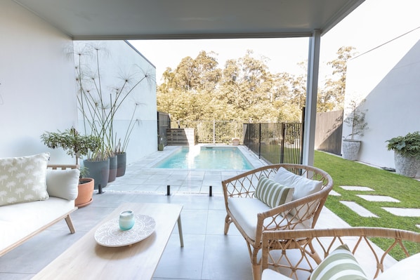 A covered outdoor area with a pool, seating, and potted plants.