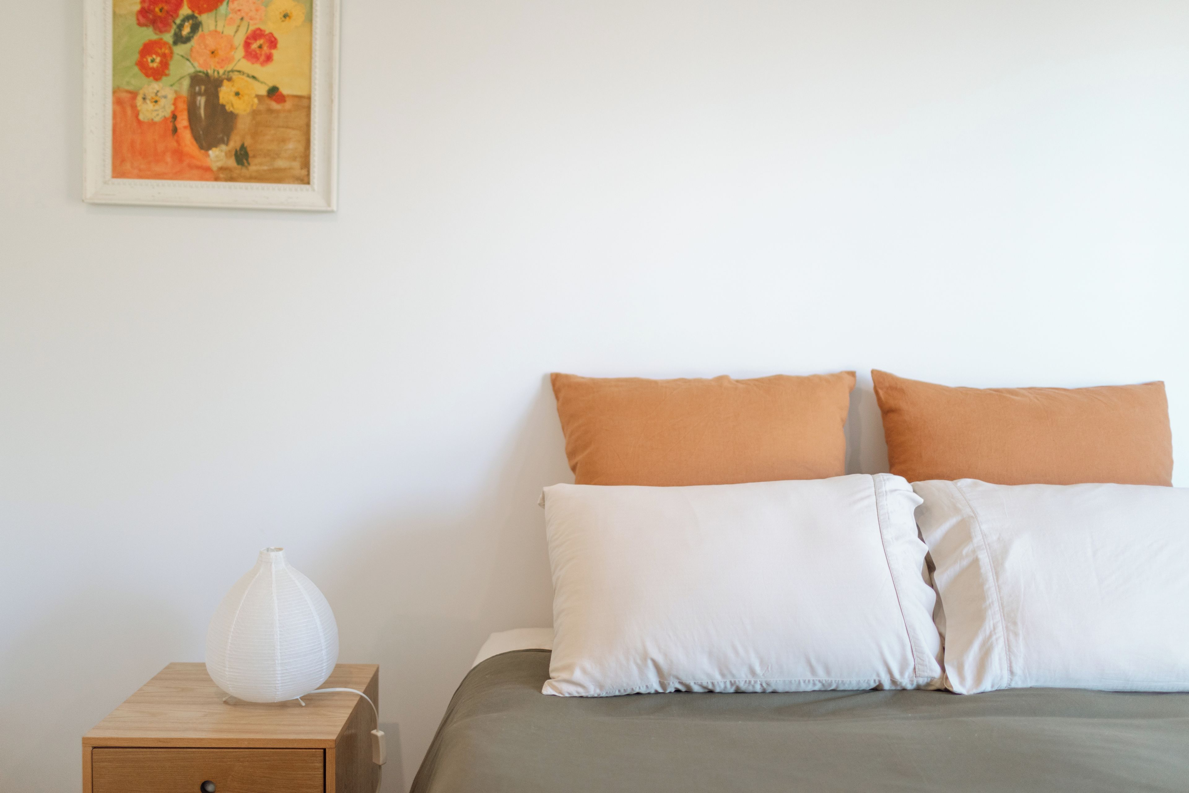 Ein Schlafzimmer mit einem Bett, Kissen, einem Nachttisch, einer Lampe und einem Bild an der Wand.