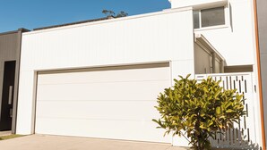 Um edifício moderno branco com porta de garagem, uma pequena janela e um vaso de planta.
