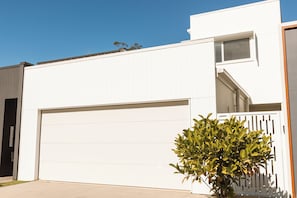 Un bâtiment moderne de couleur blanche, doté d’une porte de garage, d’une petite fenêtre et d’un pot de fleurs.