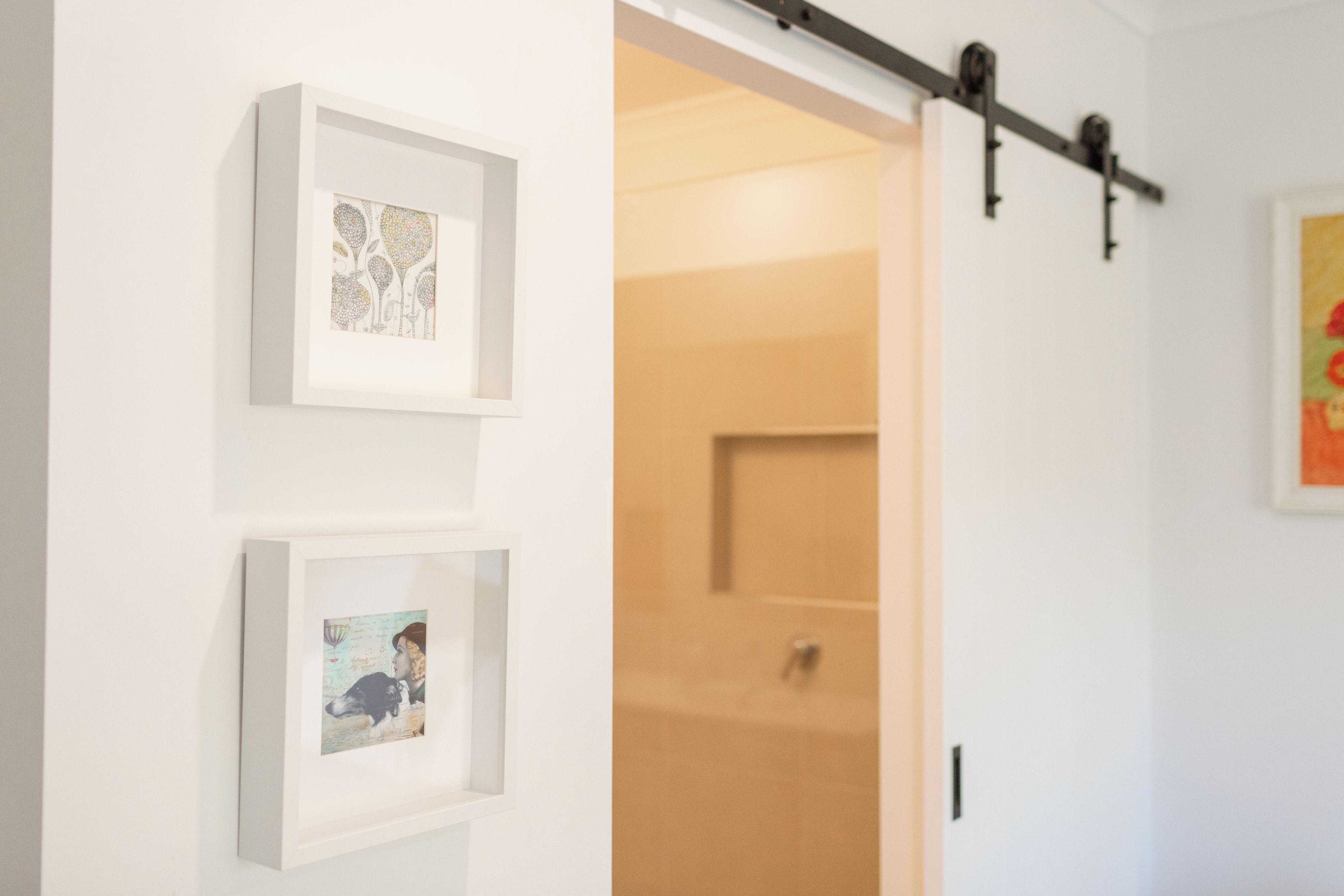 Een gang met ingelijste kunstwerken aan de wanden en een schuifdeur naar een andere kamer.