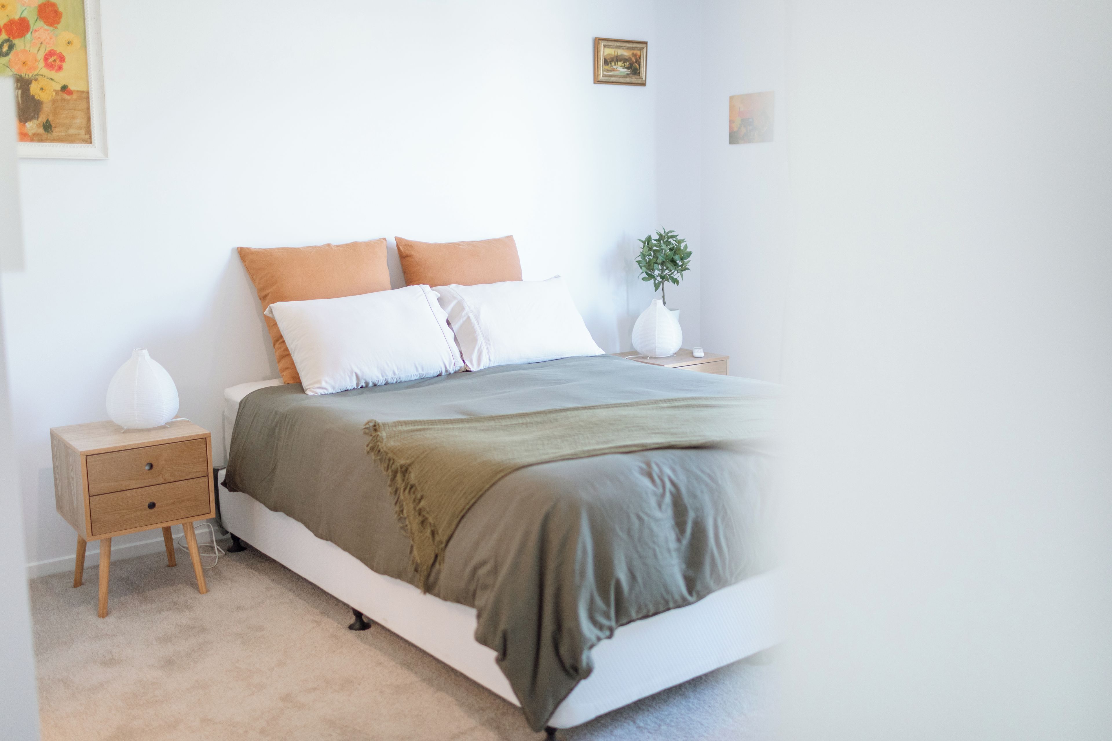 A bedroom with a bed, bedside tables, a nightstand, a lamp, and a wall-mounted picture.