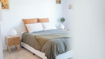 A bedroom with a bed, bedside tables, a nightstand, a lamp, and a wall-mounted picture.
