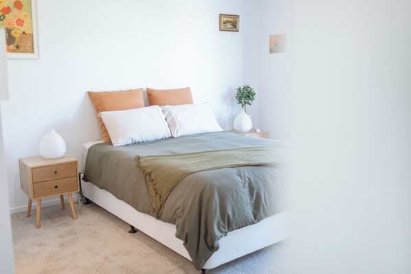 A bedroom with a bed, bedside tables, a nightstand, a lamp, and a wall-mounted picture.