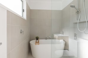 A modern bathroom with a freestanding bathtub, a showerhead, and a small potted plant.