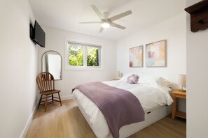Une chambre à coucher avec un lit, une chaise, une fenêtre, un ventilateur de plafond et des œuvres d’art accrochées au mur.