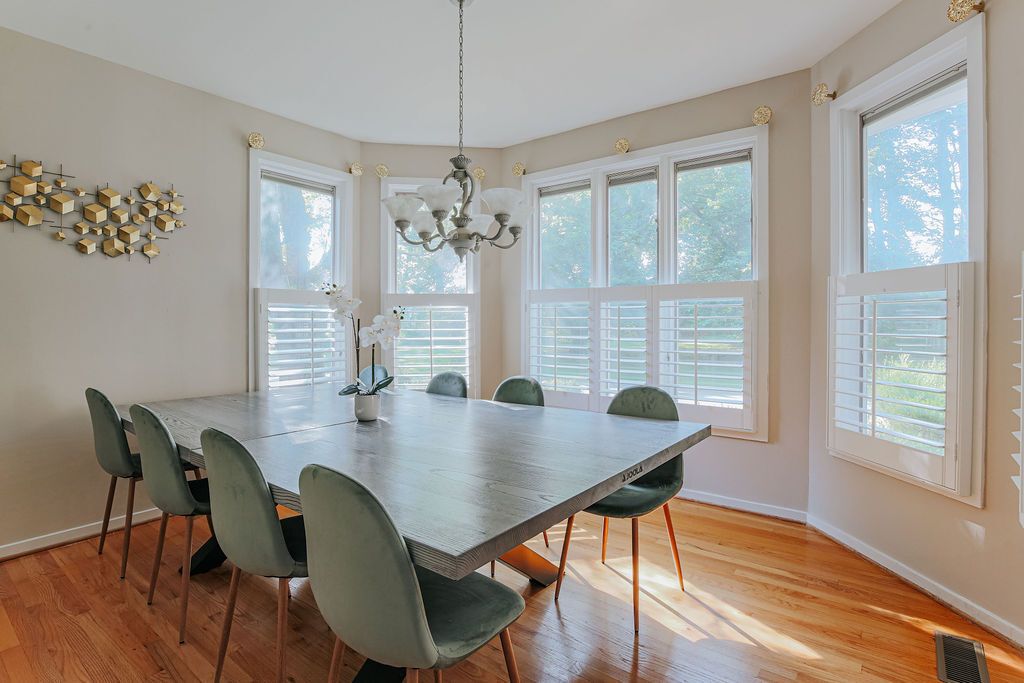 A dining room with a large table, six chairs, a chandelier, and large windows.