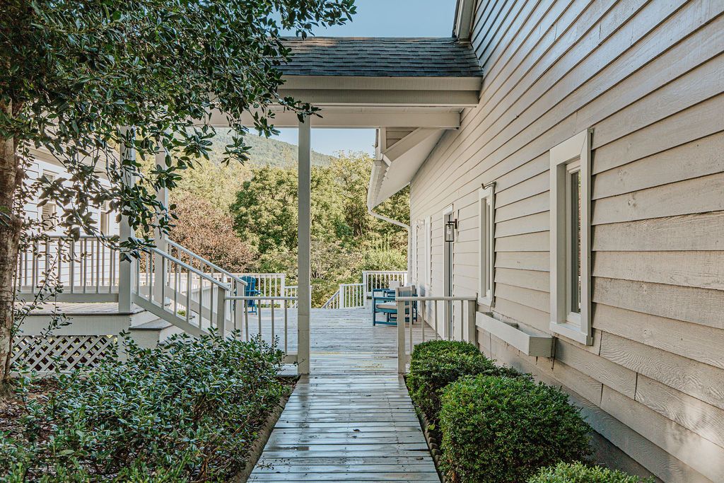 A wooden deck leading to a house with a covered porch and a view of a mountainous landscape.