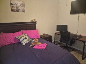 Ein Schlafzimmer mit einem Bett, einem Schreibtisch, einem Sessel, einem Fernseher und einem Teddybären.