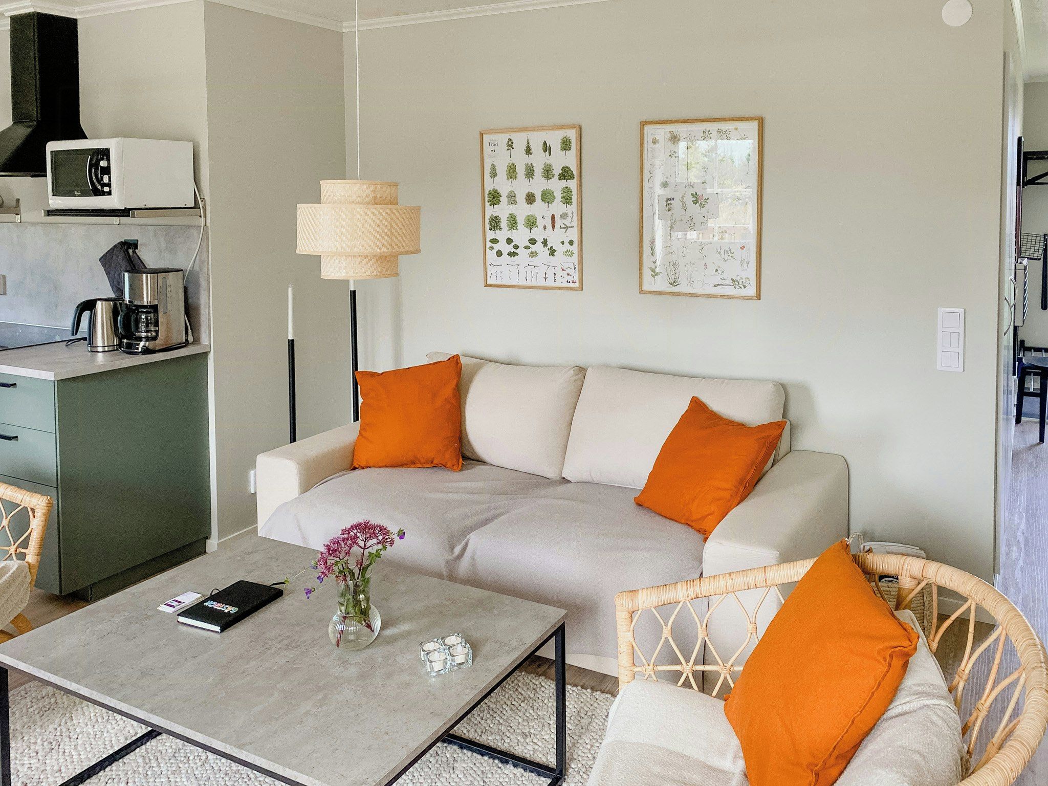 A modern living room with a sofa, coffee table, and two chairs. There is a kitchen area with a microwave and a coffee maker.