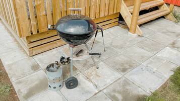Ein tragbarer Grill mit Metallschornstein und zylindrischem Behälter, auf einer Beton Terrasse mit einem Holzzaun im Hintergrund.