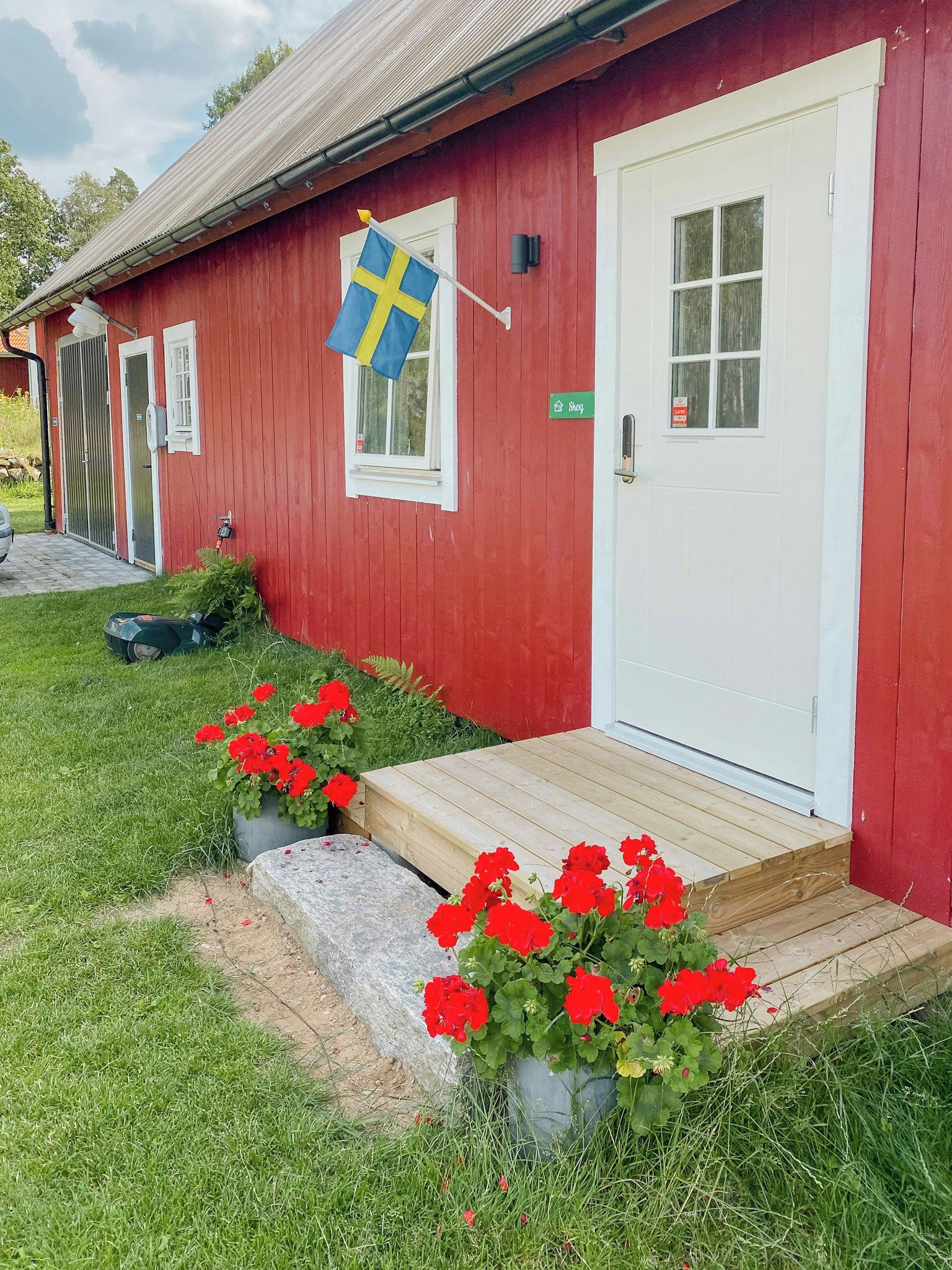A red building with a white door, a Swedish flag, and red flowers in front.