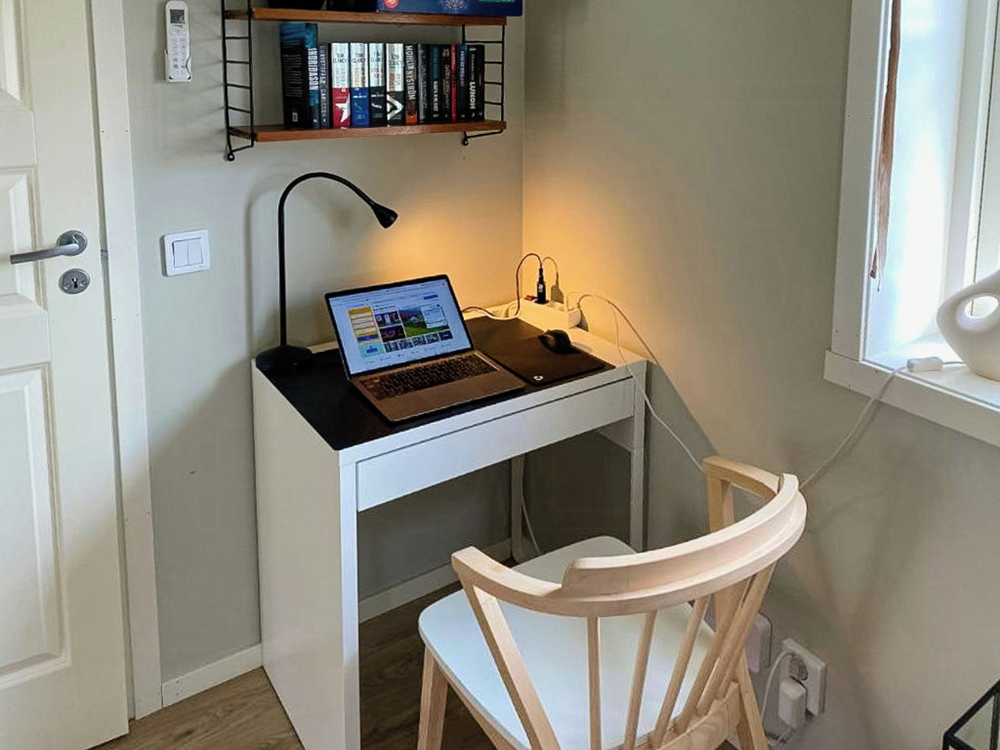 A small workspace with a laptop, a desk lamp, a chair, and a bookshelf with books.