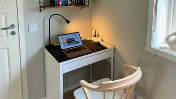 A small workspace with a laptop, a desk lamp, a chair, and a bookshelf with books.