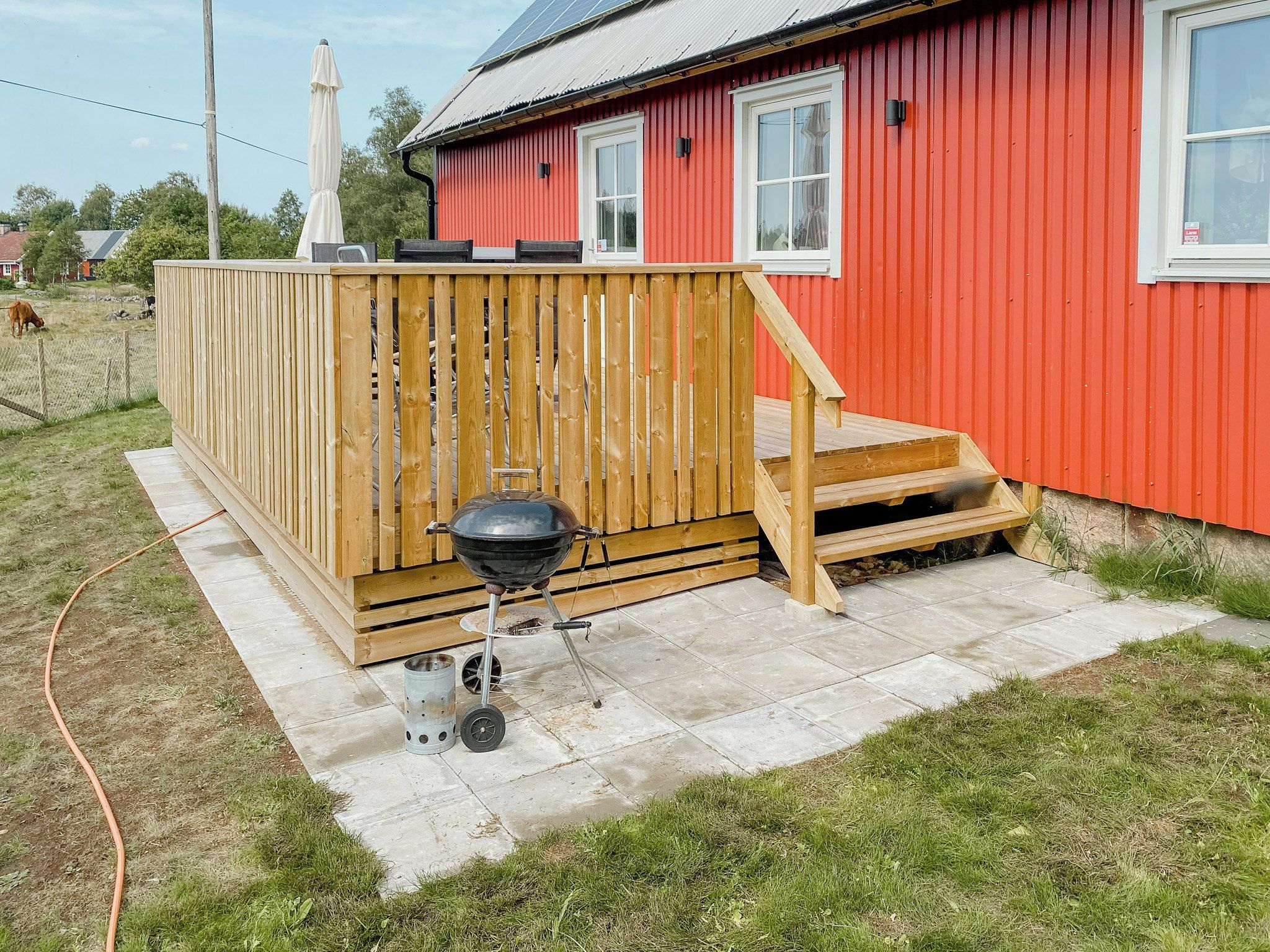 A red building with a wooden deck and a barbecue grill.