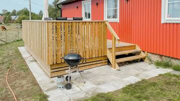 A red building with a wooden deck and a barbecue grill.