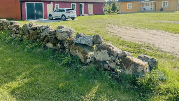 En lantlig fastighet med en röd lada, en vit bil parkerad framför och en stenmur.