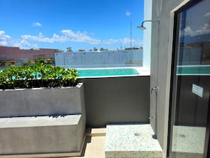 A balcony with a pool, a concrete bench, and a glass door. - Trendy Studio Near 5th Ave & Beach | Rooftop Pool (Playa del Carmen)