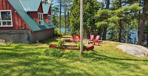 A cabin with a green roof, surrounded by a grassy yard and a lake.