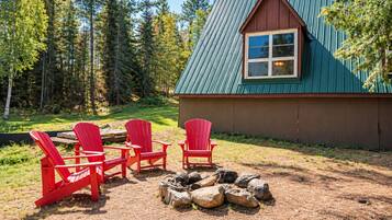 Une cabane avec un toit végétalisé, un revêtement extérieur en bois et un petit porche agrémenté de chaises Adirondack rouges.