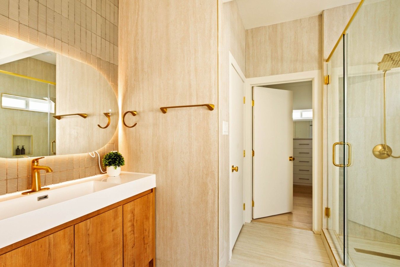 A modern bathroom with a large mirror, a gold faucet, and a wooden vanity.