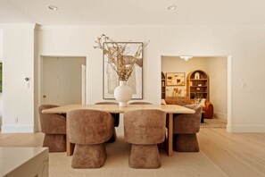 A modern dining area with a round table, six chairs, and a vase with dried branches.