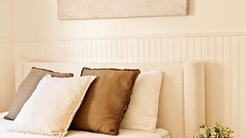 A bedroom with a bed, pillows, a round wooden side table, and a wall-mounted artwork.