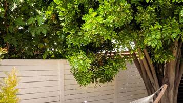A hammock under a tree in a garden with a wooden fence and flowering plants.
