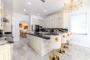 Cocina amplia con muebles blancos, encimera de mármol y taburetes dorados.