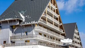 Un immeuble à plusieurs étages, doté d’un toit en pente, de balcons et surplombant un ciel dégagé.