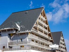 Ein mehrstöckiges Gebäude mit einem geneigten Dach, Balkonen und blauem Himmel.