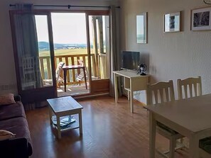 Ein Zimmer mit einer Schiebetür zum Balkon, einem kleinen Tisch, einem Fernseher auf einem Schrank und einigen Stühlen.