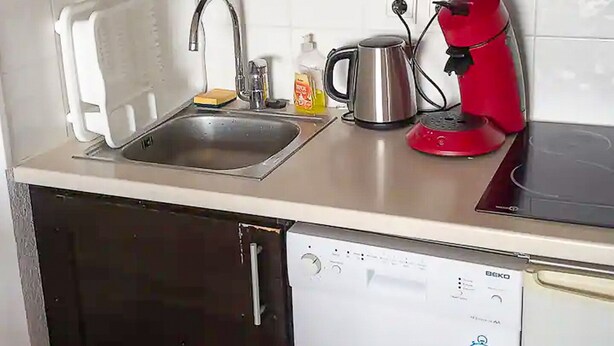 Une cuisine équipée d’un lave-vaisselle, d’un évier, d’une bouilloire et d’une cafetière rouge.