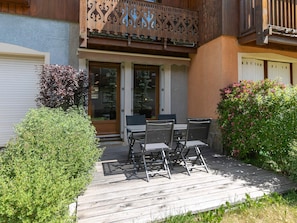 A wooden deck with a table and chairs, surrounded by greenery and a building with a balcony. - Semi-detached chalet south, shuttle to slope - 7 guests (La Salle-les-Alpes)