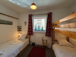 A small, cozy room with two single beds, a window with curtains, a radiator, and a small table. - Semi-detached chalet south, shuttle to slope - 7 guests (La Salle-les-Alpes)